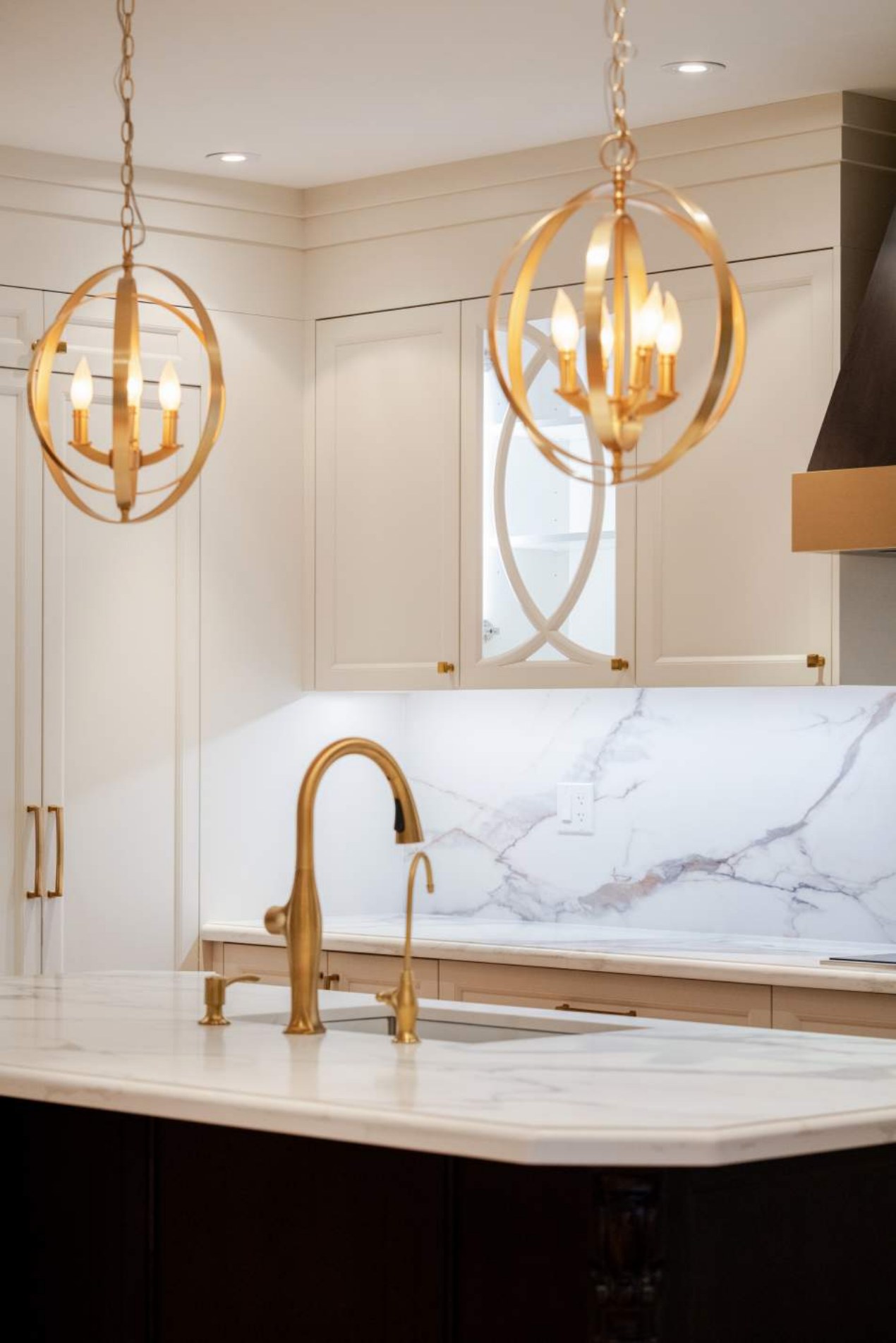 Glazed upper cabinetry detail with brass hardware and orb pendants