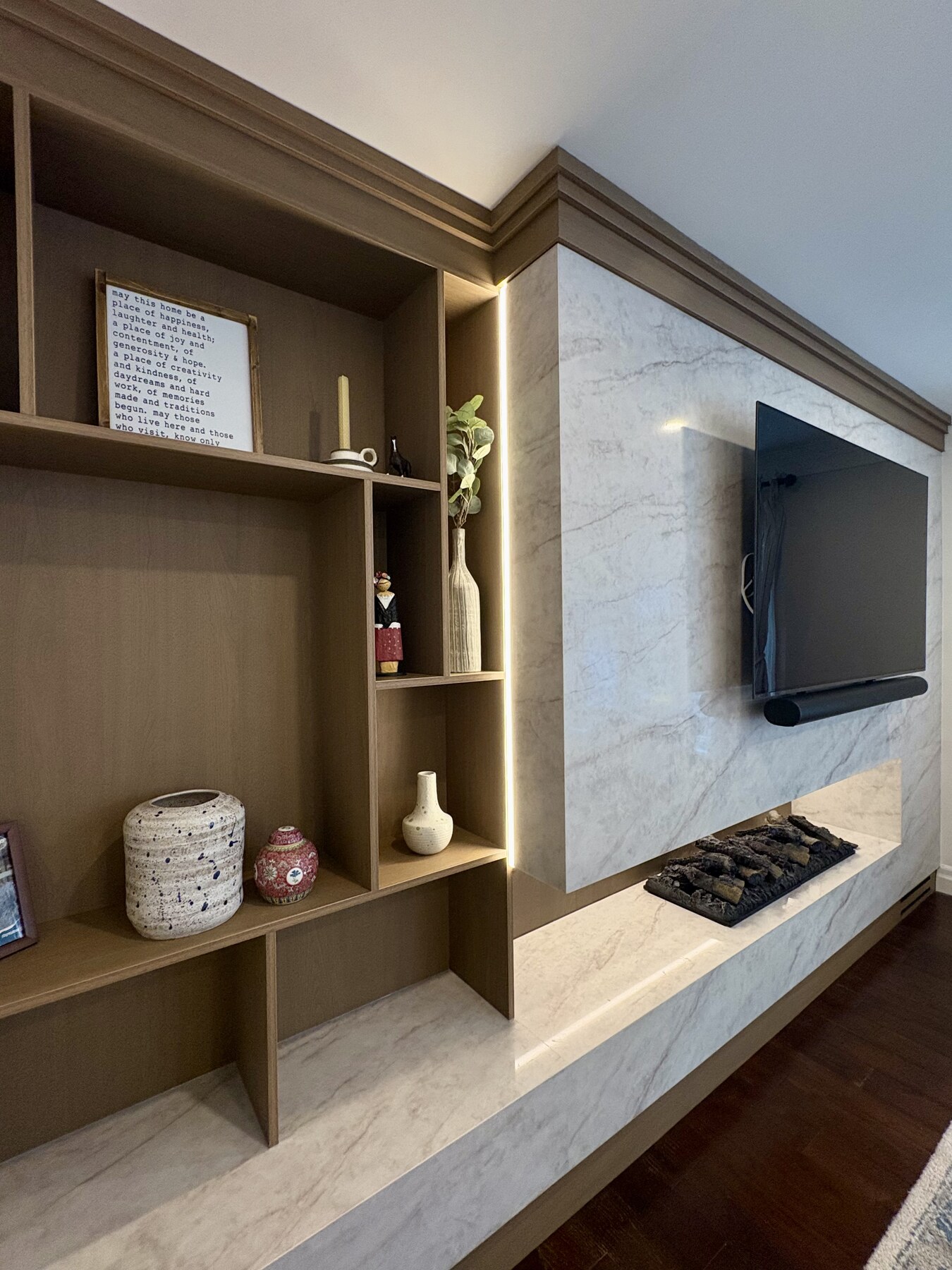 Asymmetric oak shelving with cove lighting alongside the stone fireplace wall